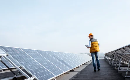 View on the rooftop solar power plant with mann walking and examining photovoltaic panels. Concept of alternative energy and its service